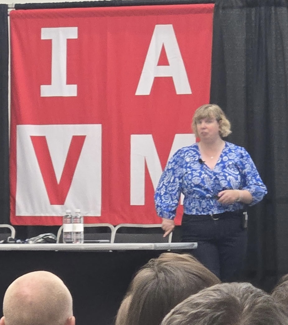 Darby giving a presentation in front of an IAVM banner